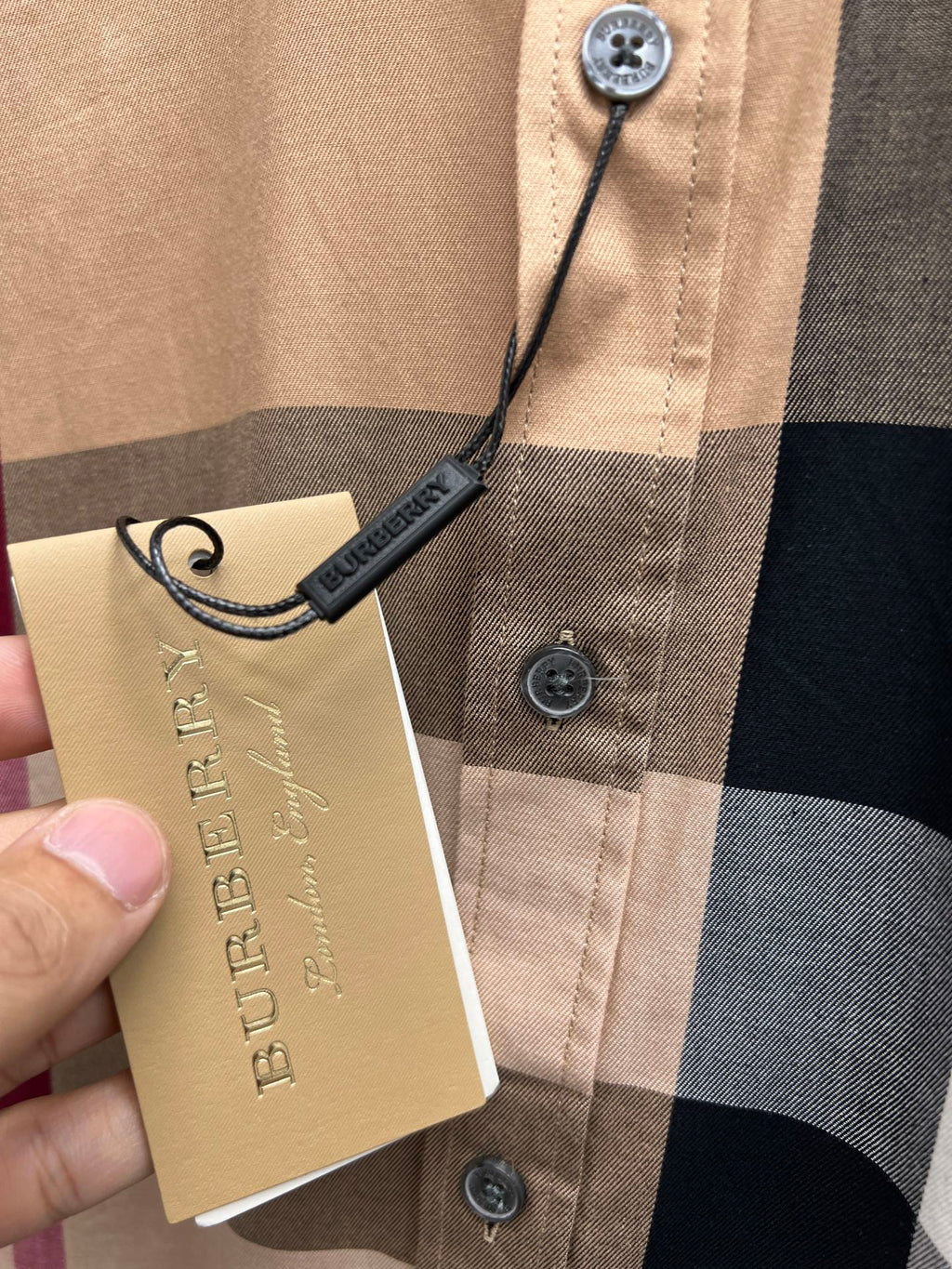 Beige plaid button-up shirt with Burberry hang tag on front