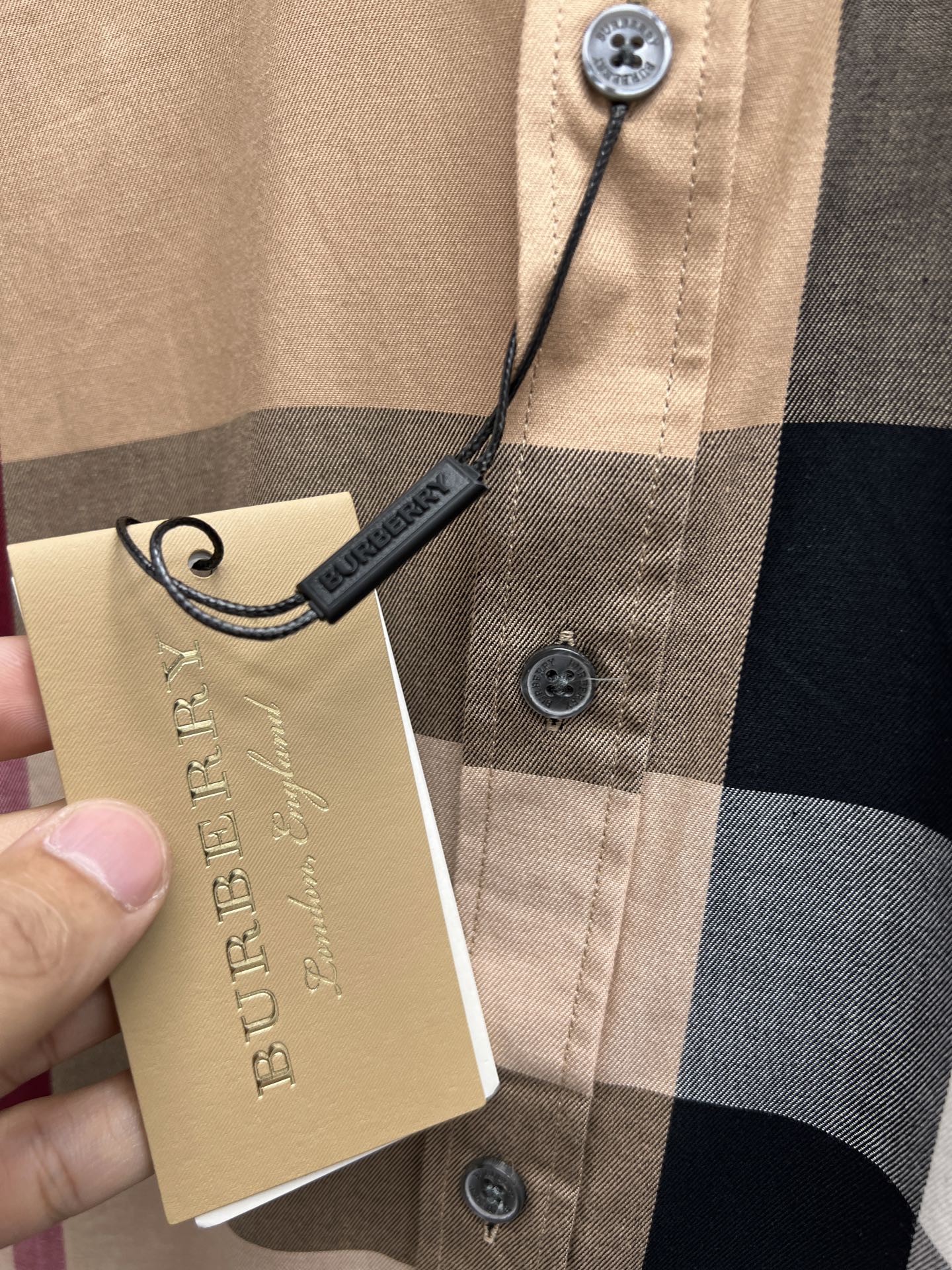 Beige plaid button-up shirt with Burberry hang tag on front