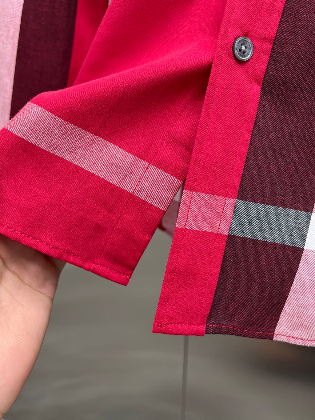 Long-sleeve shirt cuff with red plaid pattern and button detail