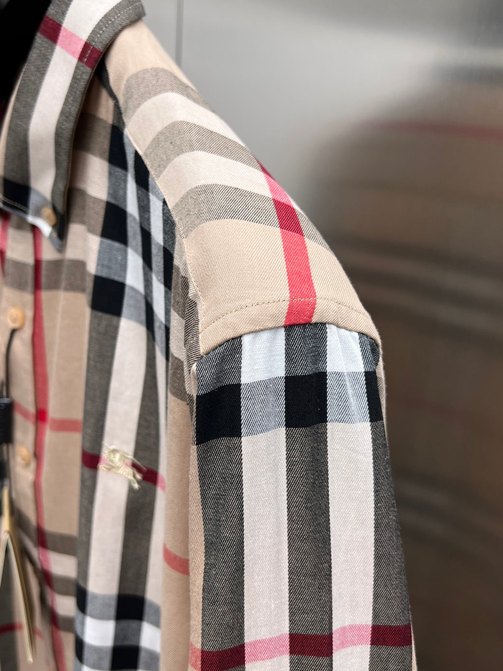 Side view close-up of plaid sleeve on beige button-up shirt with black and red