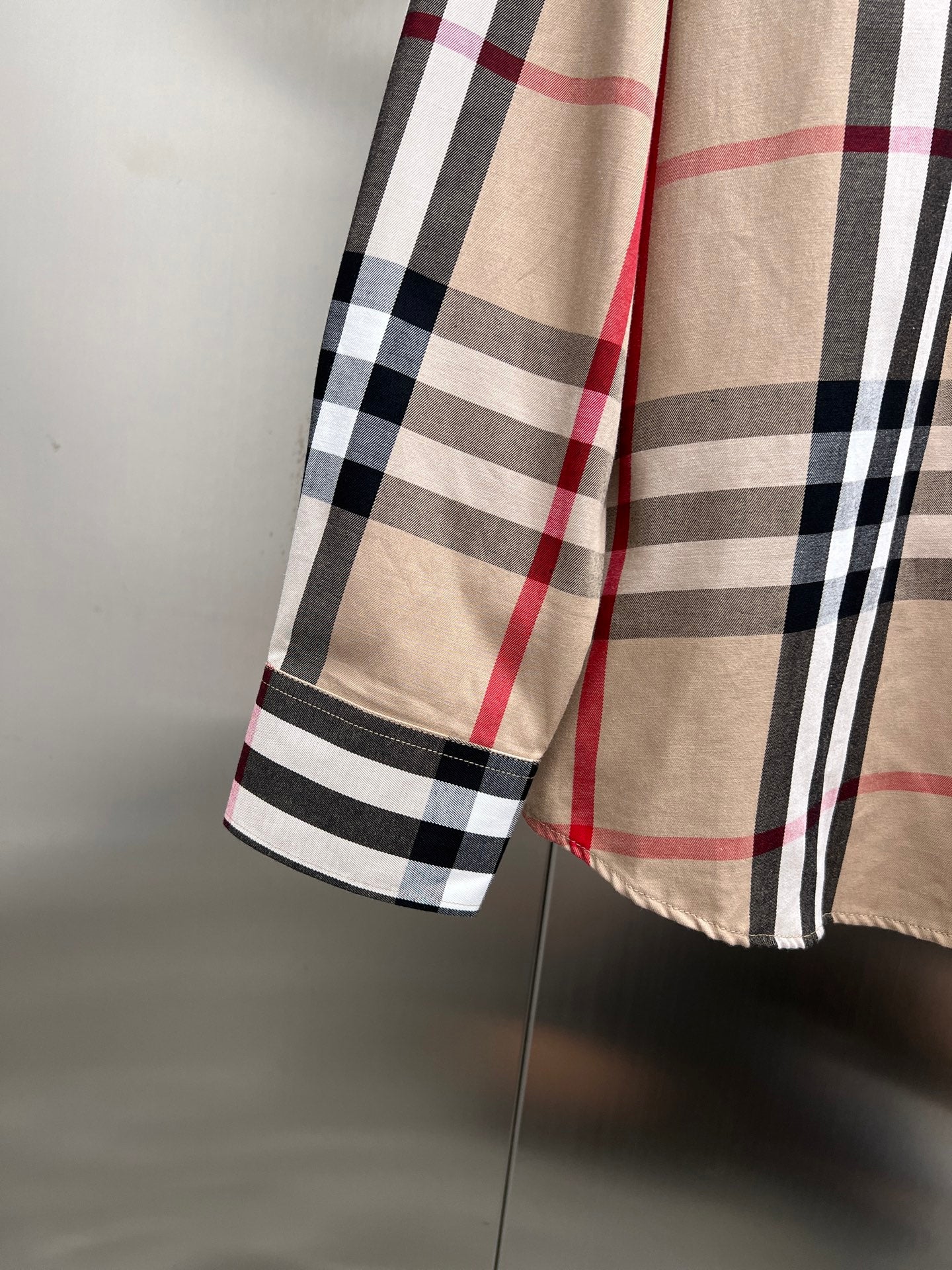 Lower sleeve and hem of plaid long-sleeve button-up shirt in beige, black, white, red