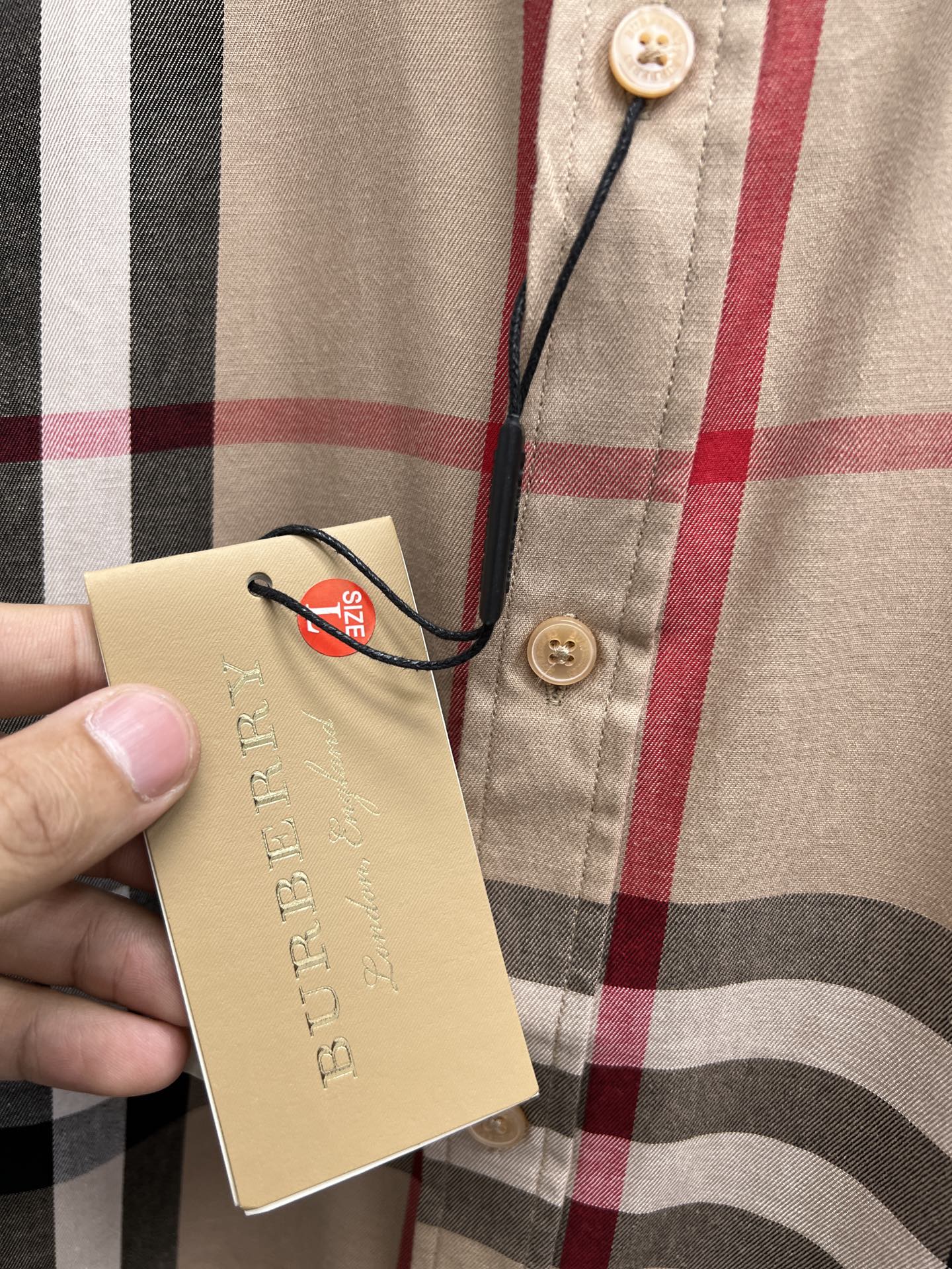 Hangtag on beige plaid button-up shirt with gold buttons at placket