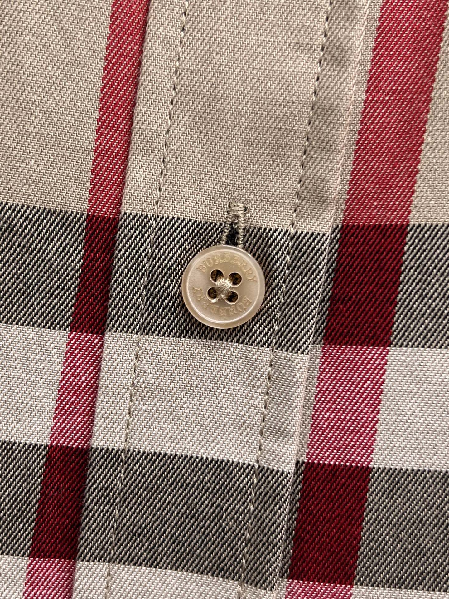 Close-up of button on beige plaid shirt placket, black white and red checks