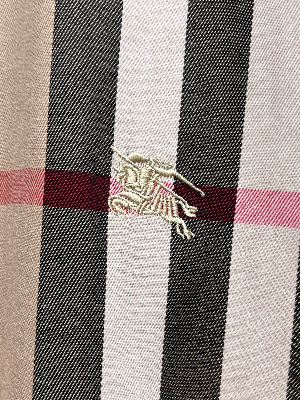 Embroidered logo detail on plaid shirt fabric, beige with black white and red