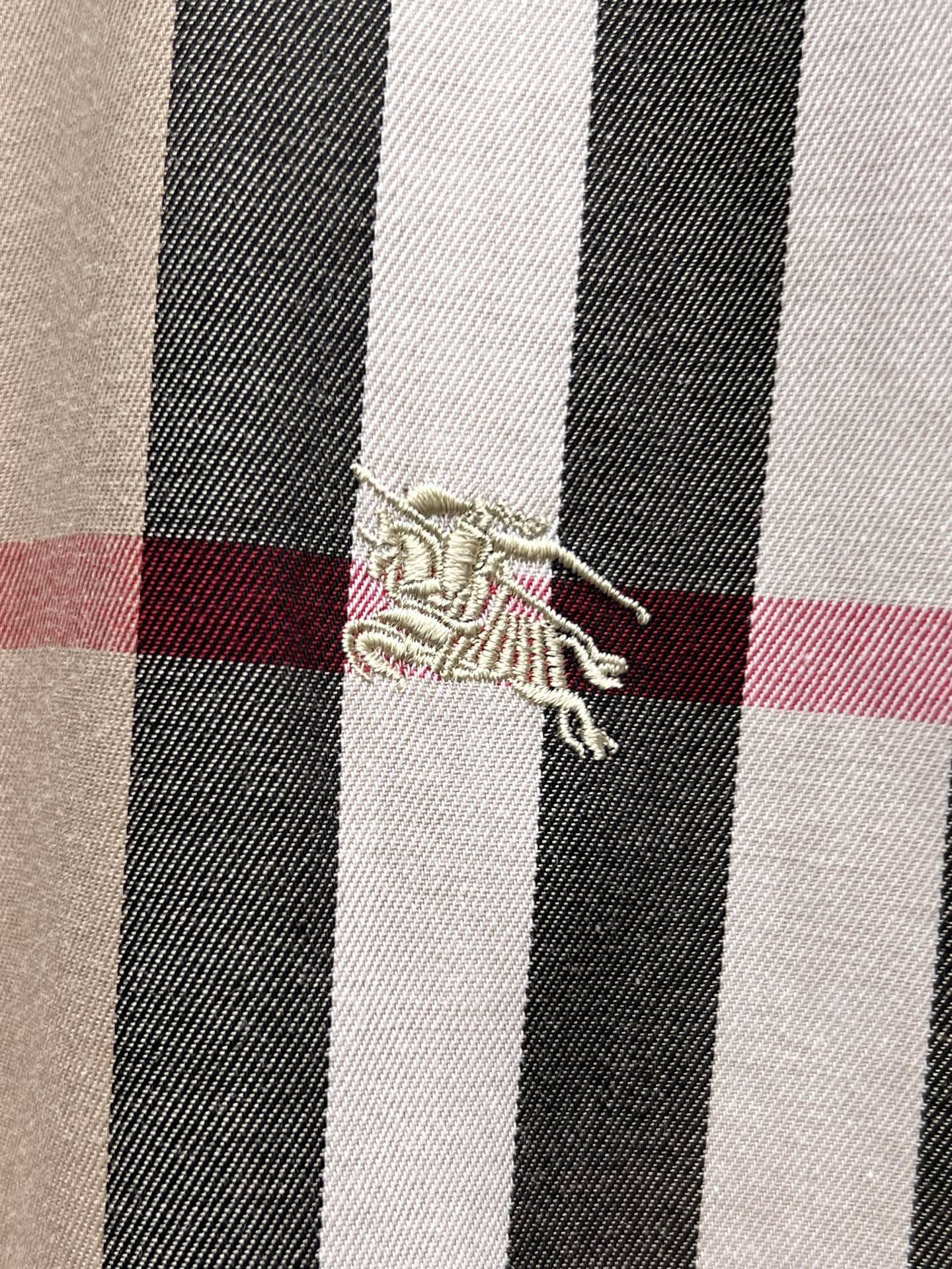 Embroidered logo detail on plaid shirt fabric, beige with black white and red