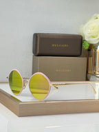 Round eyeglasses with gold frame, mirrored yellow lenses, and pink side accents