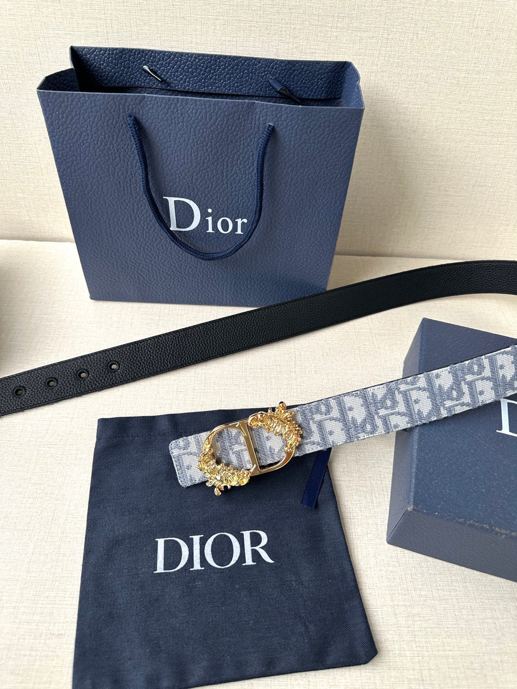 Blue-gray logo jacquard belt with gold medallion buckle on dark leather strap