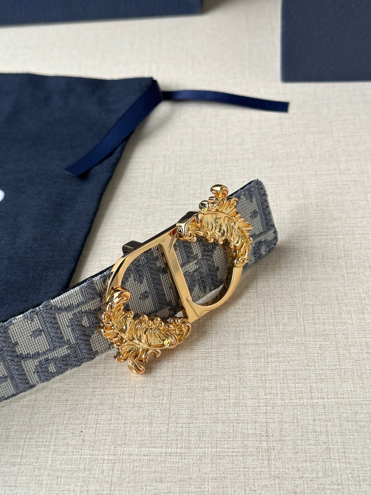 Blue-gray logo jacquard belt with large gold buckle and engraved center