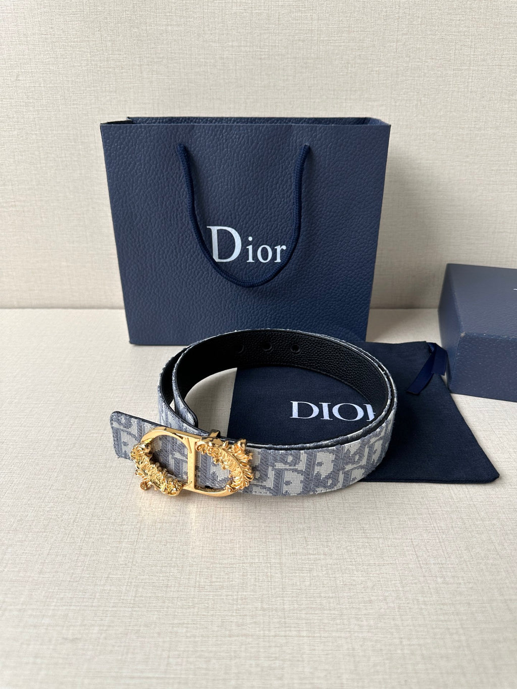 Blue-gray logo jacquard belt with ornate gold buckle and dark leather strap