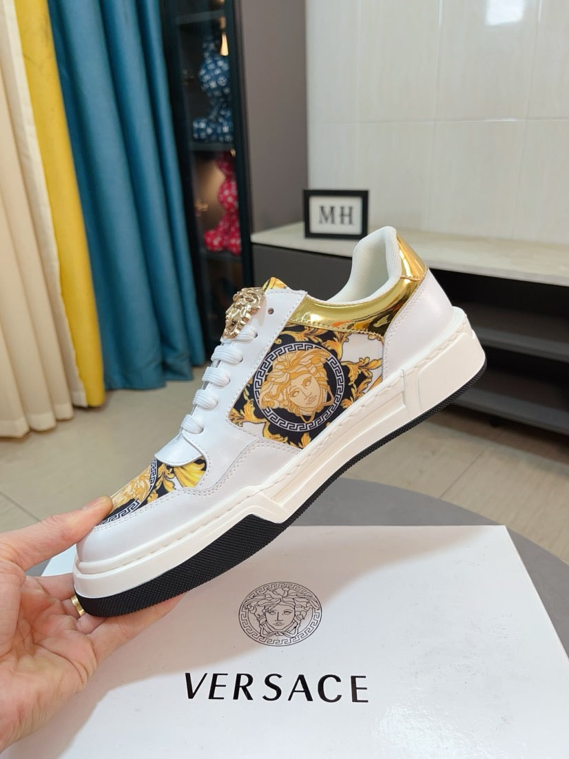White low-top lace-up sneakers with gold baroque medallion patch and gold-trim details.