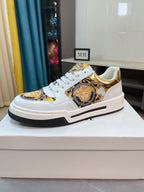 White low-top lace-up sneakers with gold baroque medallion patch and black-striped sole.