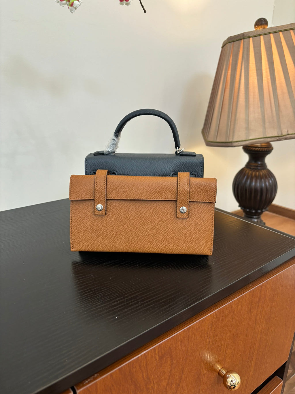 Hermes bag in tan with top handle, front flap, and silver clasp hardware.