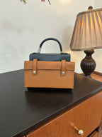 Hermes bag in tan with top handle, front flap, and silver clasp hardware.