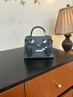 Hermes bag in dark blue with top handle, front flap, and silver emblem accents.