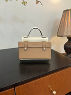Tan leather handbag with top handle and structured front panel, metal feet