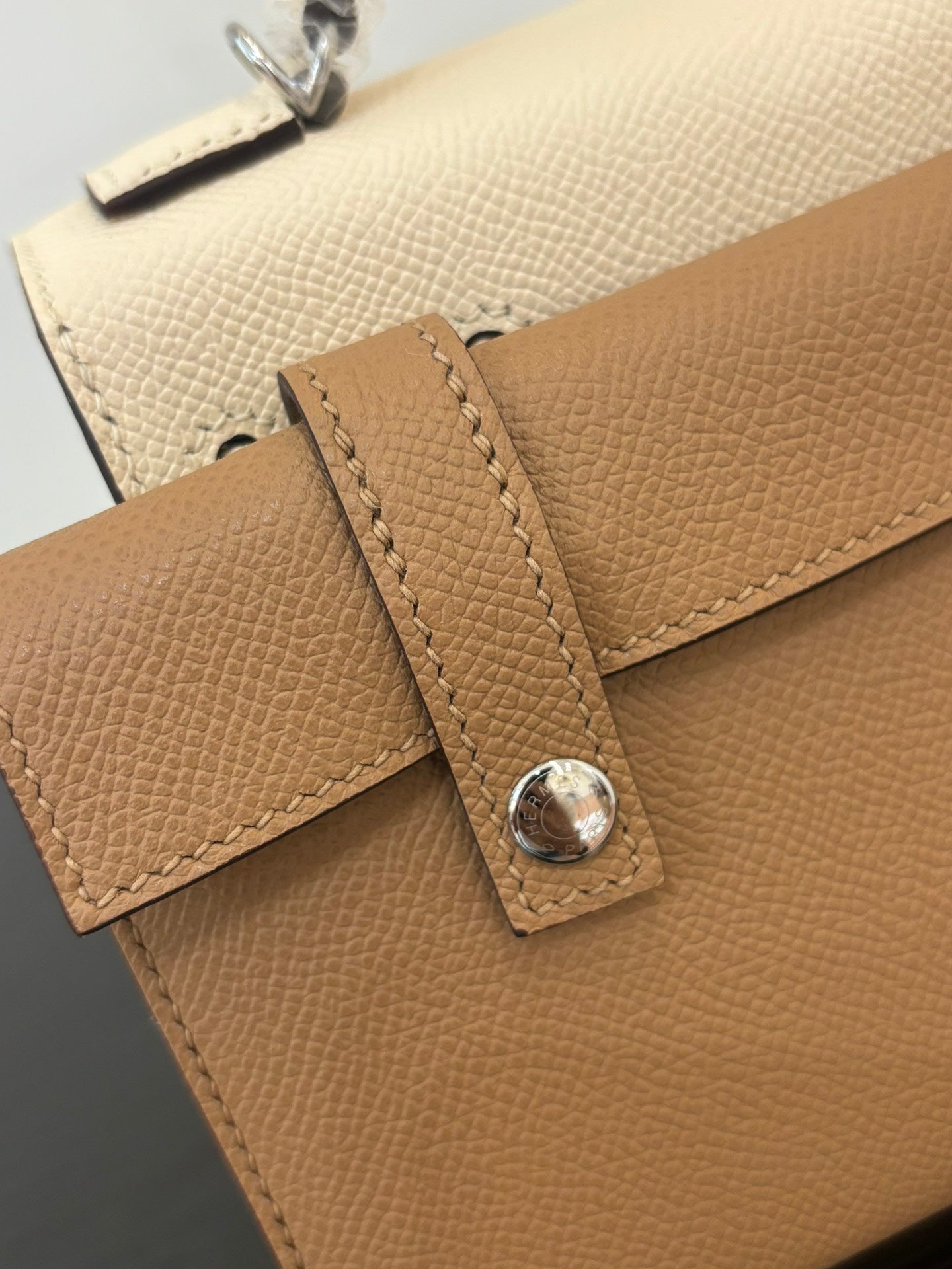 Close-up of tan leather handbag strap with stitched tab and silver-tone snap clasp