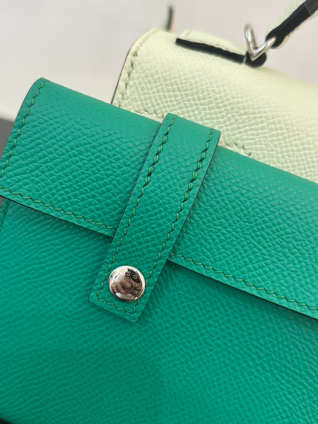 Hermes bag close-up of teal flap with round button clasp and stitched trim