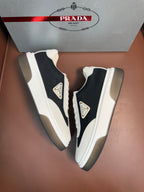 Prada unisex sneakers, white and black colorblock with gold-tone logo patch on side.