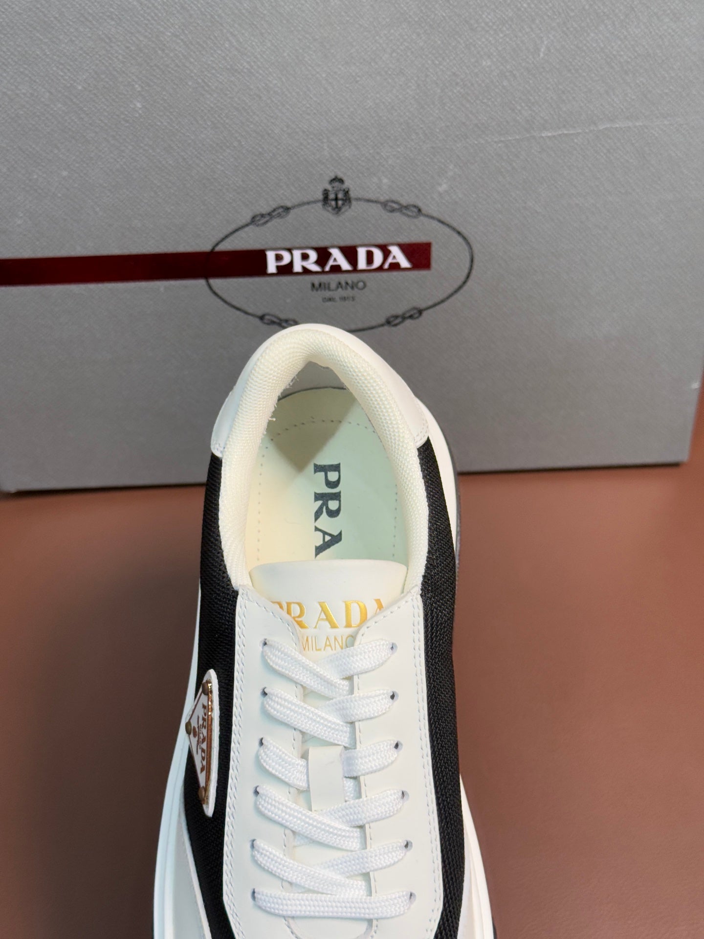 Prada unisex sneaker tongue and lace area, white with Prada logo embroidery.