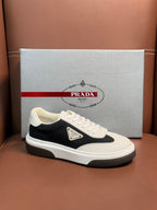 Prada unisex sneakers, white upper with black side panel and gold-tone logo patch.