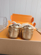 Louis Vuitton metallic gold sneakers viewed from the toe, showing white lace loops