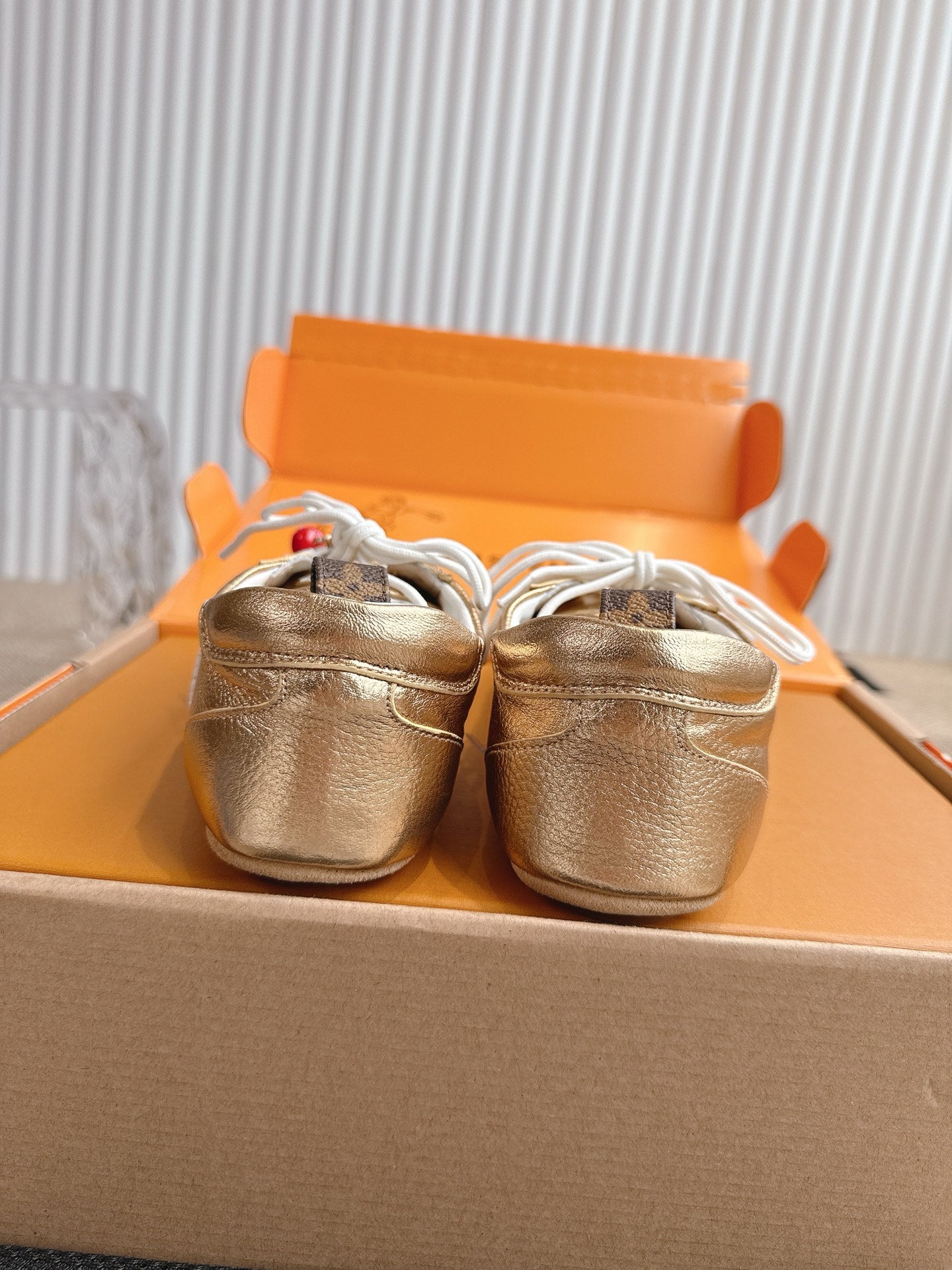 Louis Vuitton metallic gold sneakers viewed from the toe, showing white lace loops