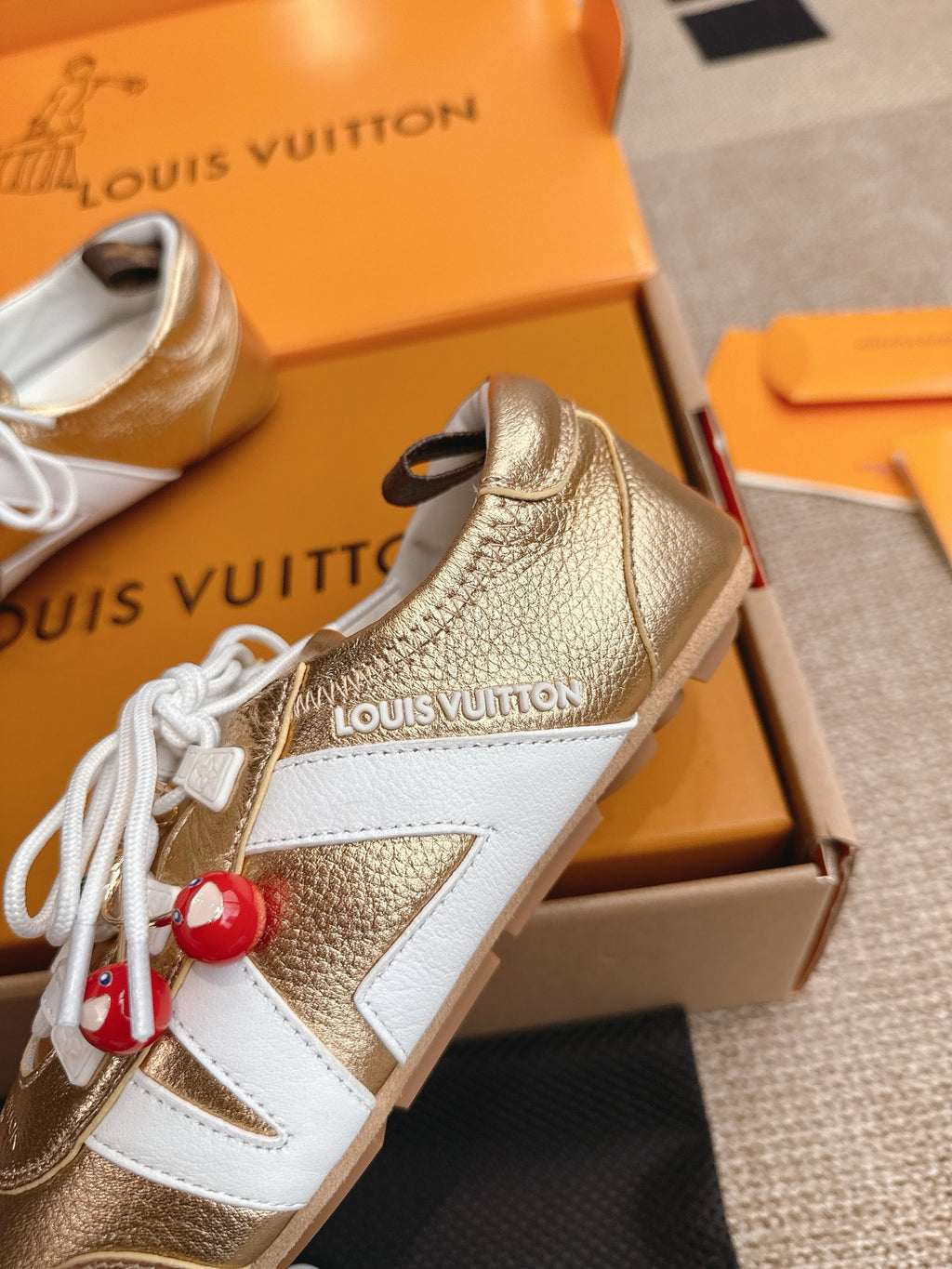 Louis Vuitton metallic gold sneaker detail with white panels, laces, and cherry charm