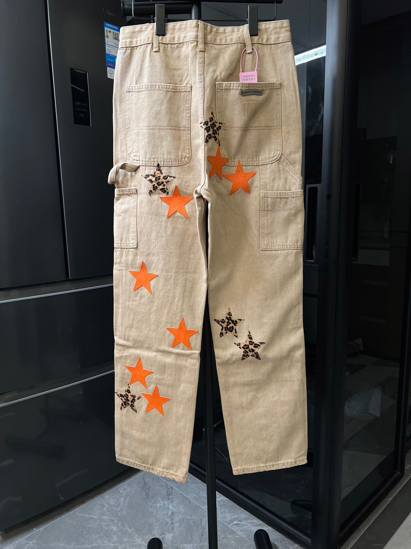 Beige wide-leg cargo pants with multiple orange star and leopard-pattern star appliques.