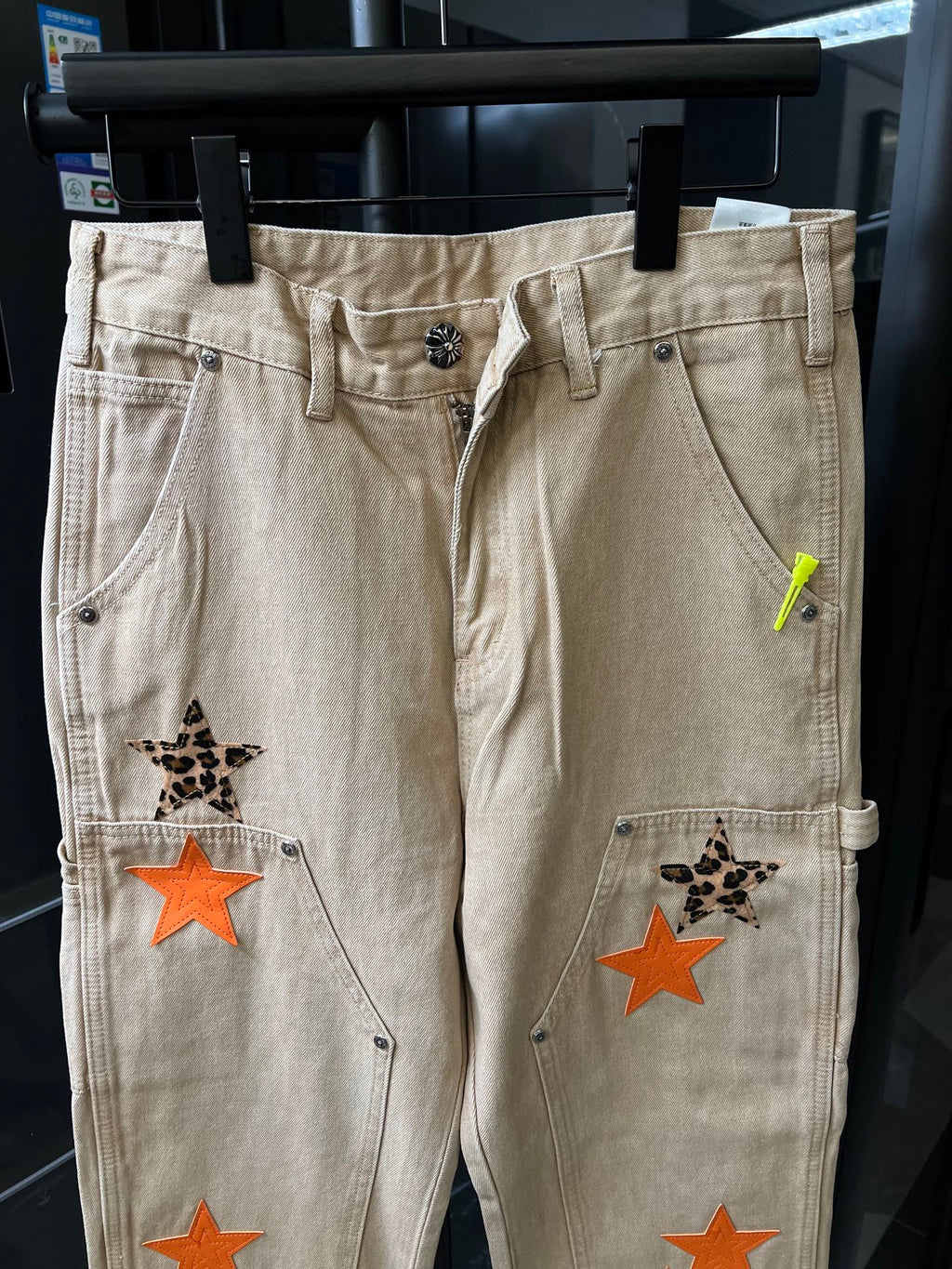 Beige cargo pants with front button closure, belt loops, and orange star patch accents.