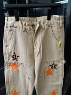 Beige cargo pants with front button closure, belt loops, and orange star patch accents.
