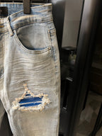 Light-wash denim jeans with curved front pocket and a large ripped knee patch