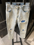 Denim jeans in light wash with knee rips and layered distressed patches