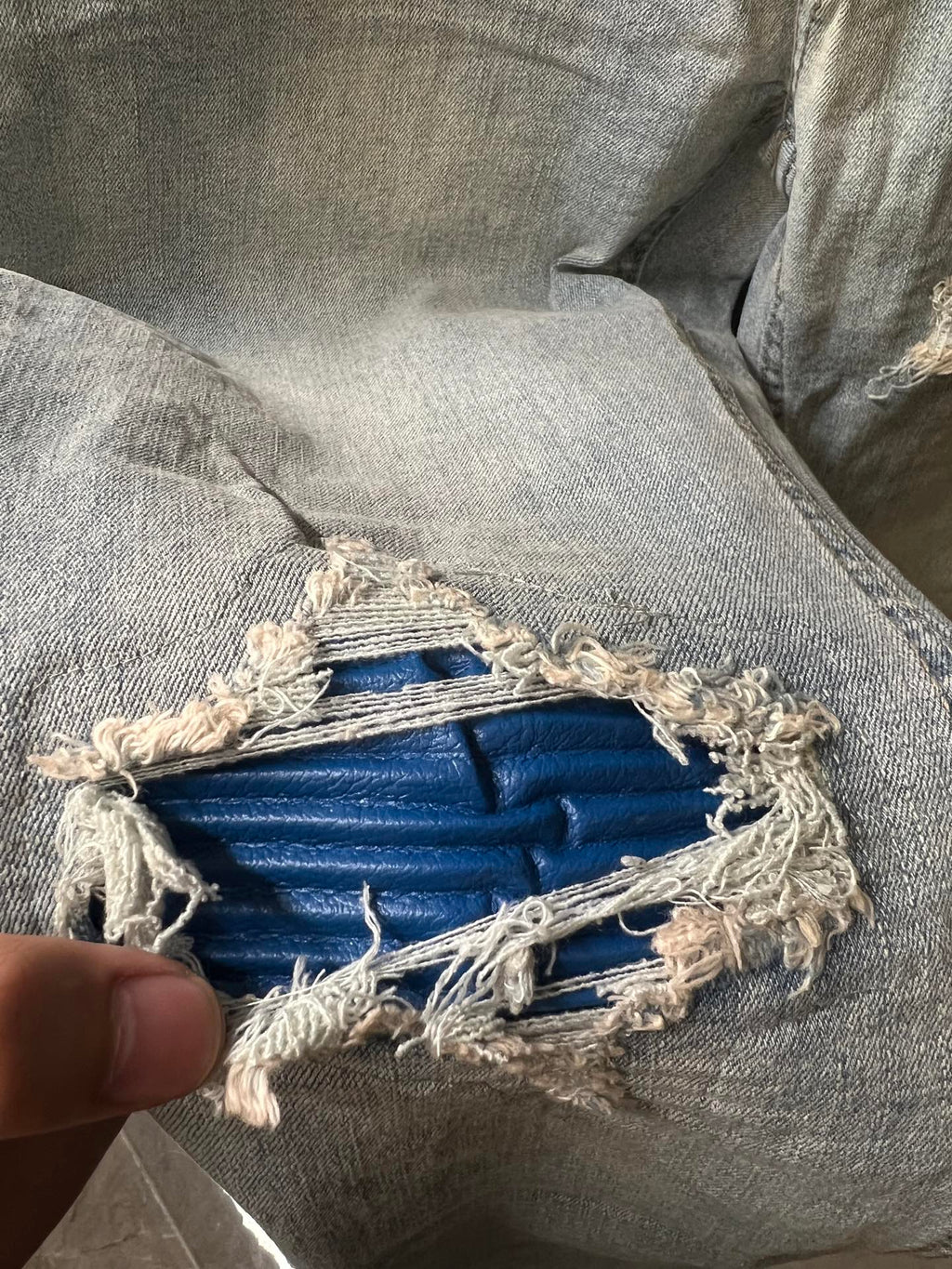 Distressed denim knee patch with exposed blue lining and frayed edges