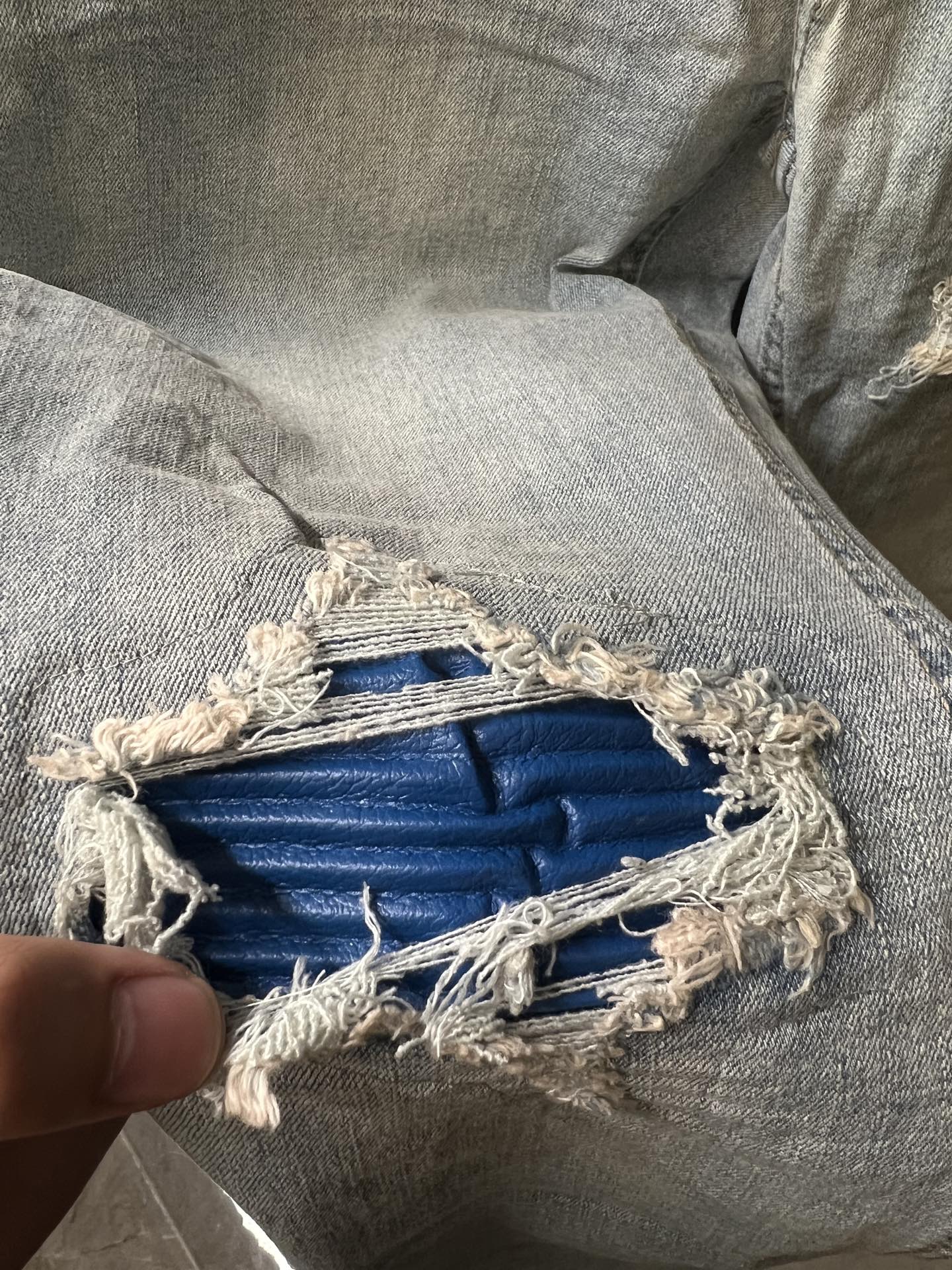Distressed denim knee patch with exposed blue lining and frayed edges