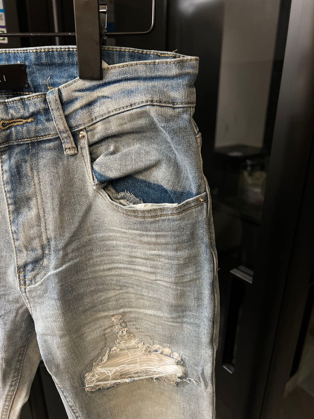 Light wash jeans with a large front pocket opening and a ripped knee patch