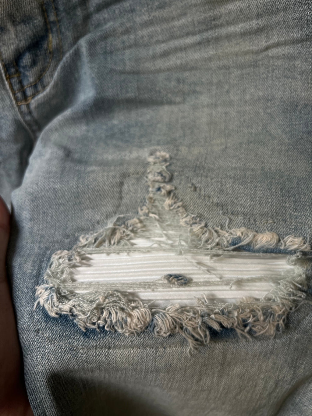 Frayed embroidered patch on distressed denim at the knee with layered threads