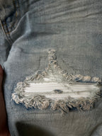 Frayed embroidered patch on distressed denim at the knee with layered threads