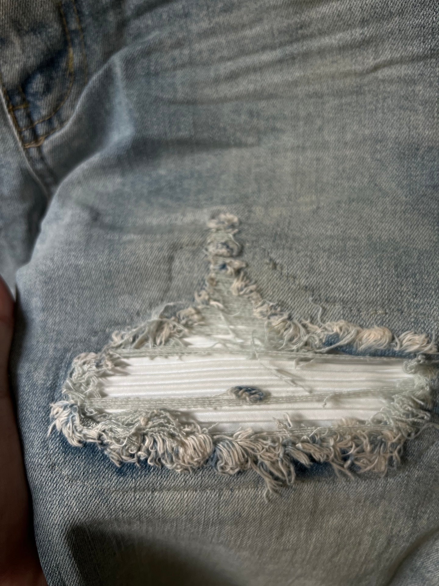 Frayed embroidered patch on distressed denim at the knee with layered threads