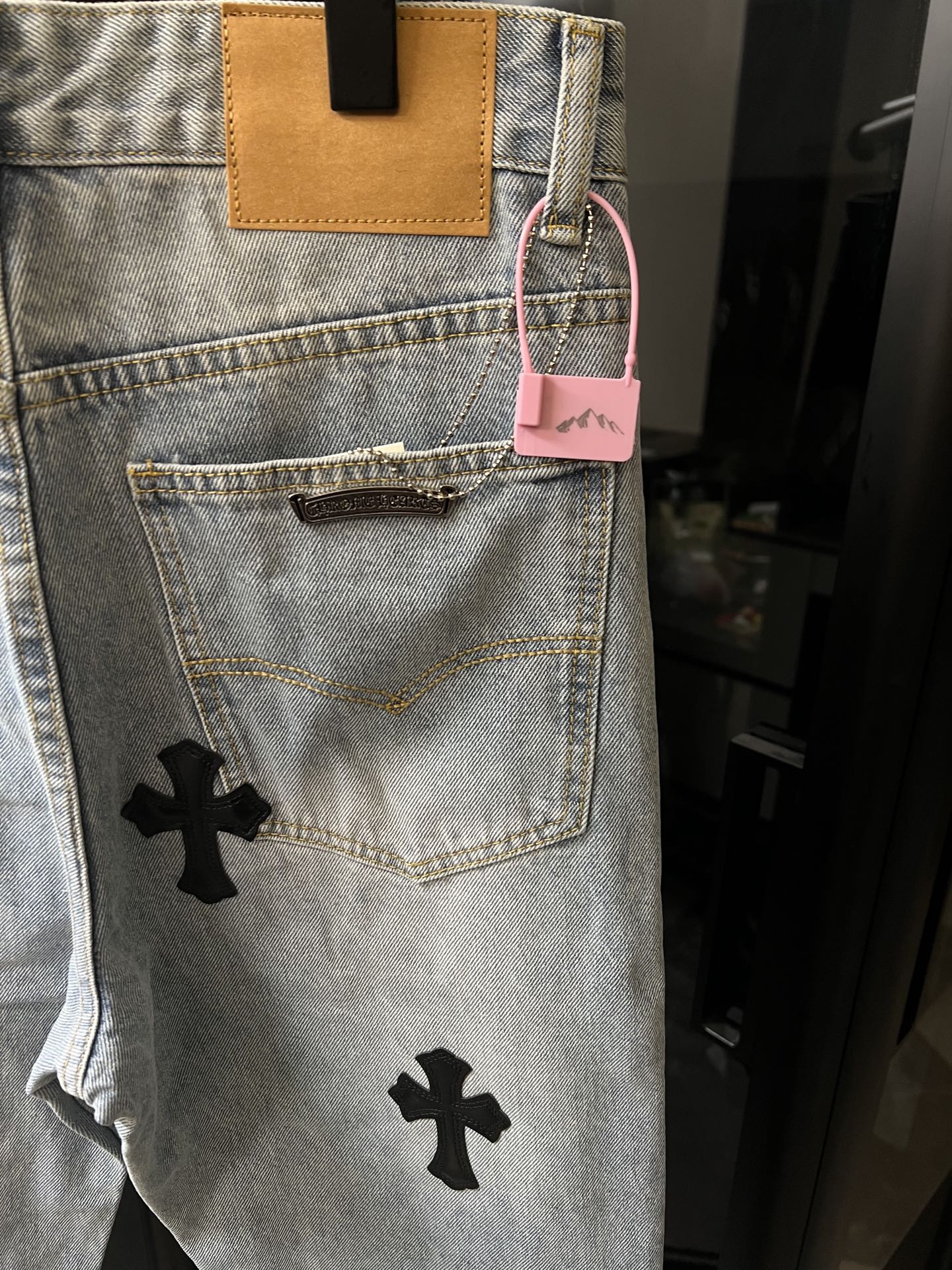 Light wash denim pants with back pocket and pink hang tag, black cross patch
