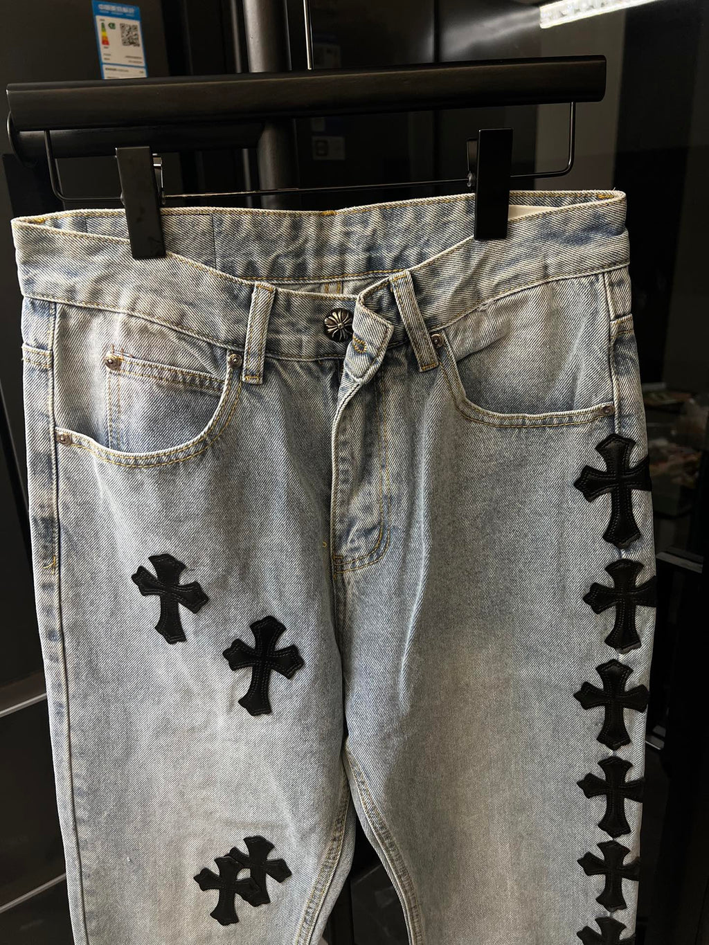 Light wash denim pants with black cross patches, belt loops and button fly