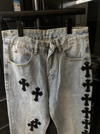 Light wash denim pants with black cross patches, belt loops and button fly