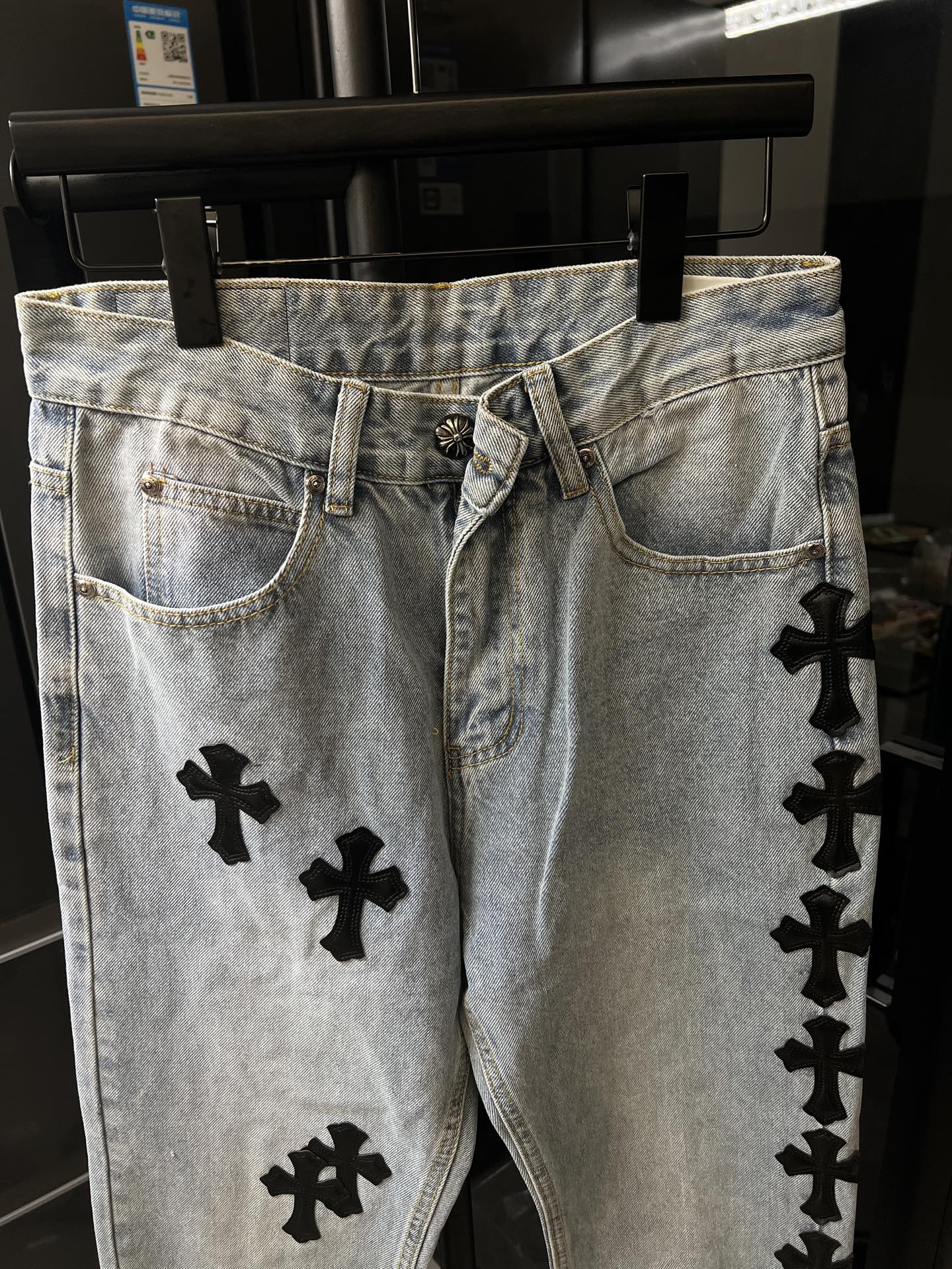 Light wash denim pants with black cross patches, belt loops and button fly