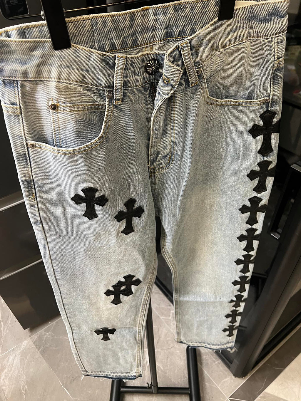 Denim pants with button fly and black cross patches along side seams