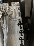 Light wash denim pants with black cross patch detail on thigh and pocket area