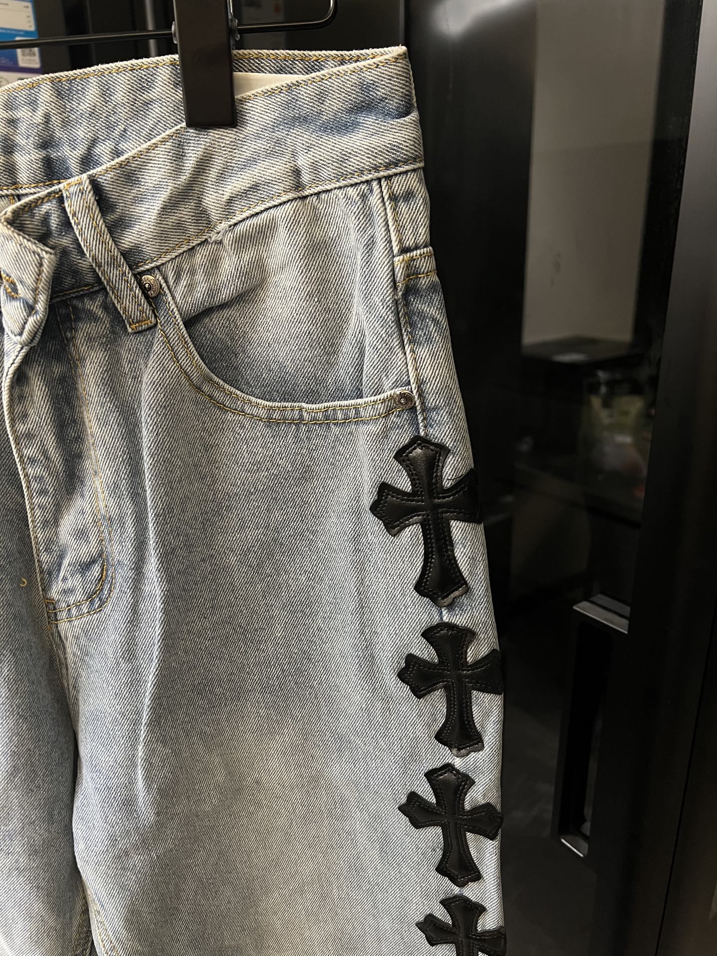 Light wash denim pants with black cross patch detail on thigh and pocket area