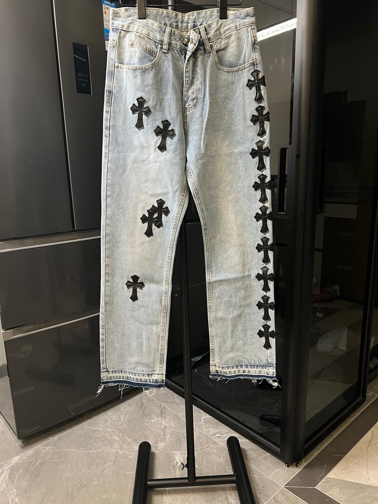 Light wash denim pants with black cross patches, button fly, straight leg