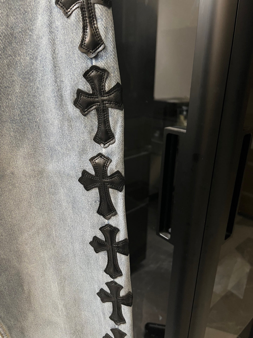 Denim pants with vertical row of black cross patches along side seam