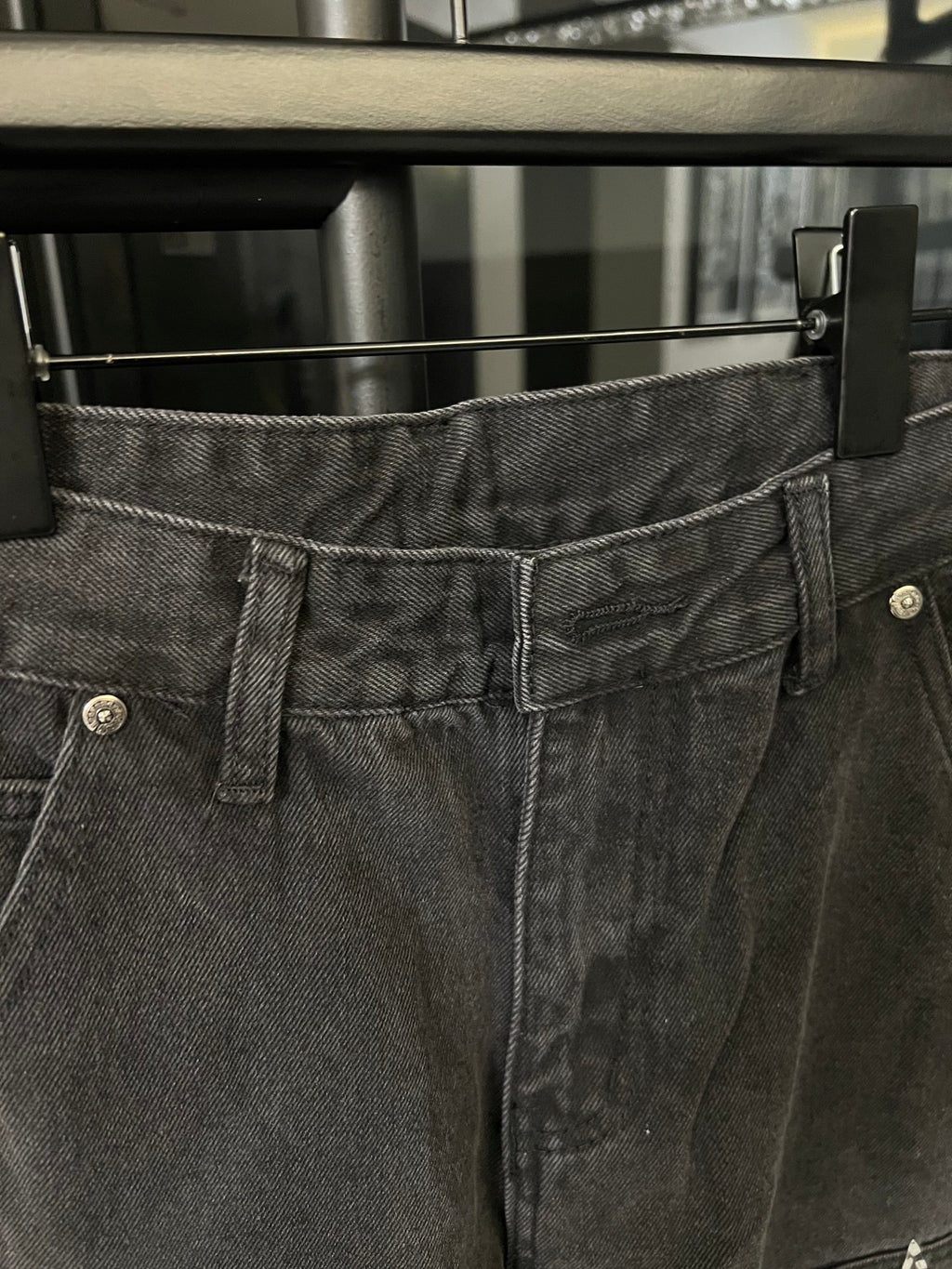 Dark gray denim pants waistband close-up with belt loops and button fly