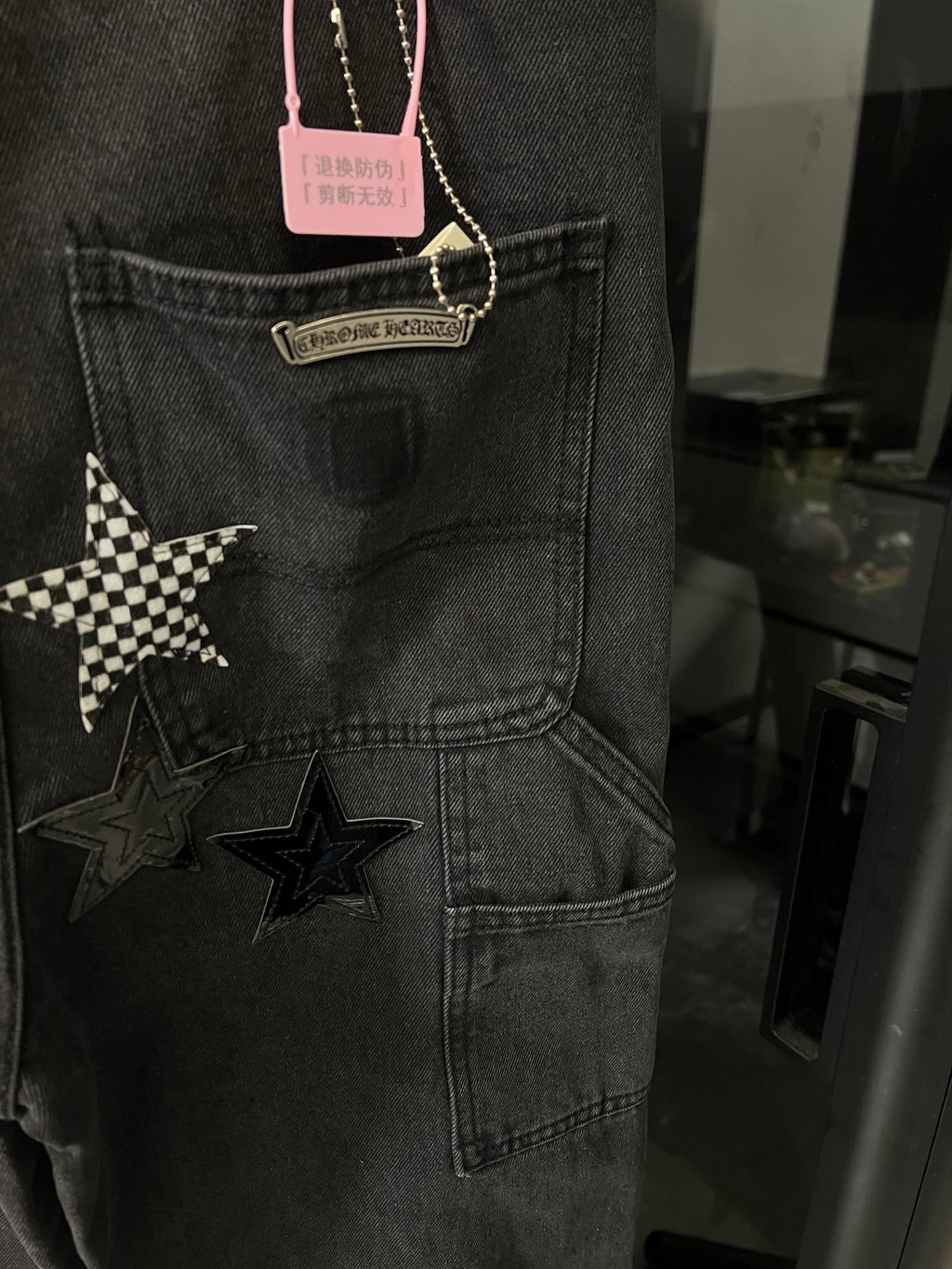 Dark gray denim pants with star appliques on cargo pocket and hanging tag