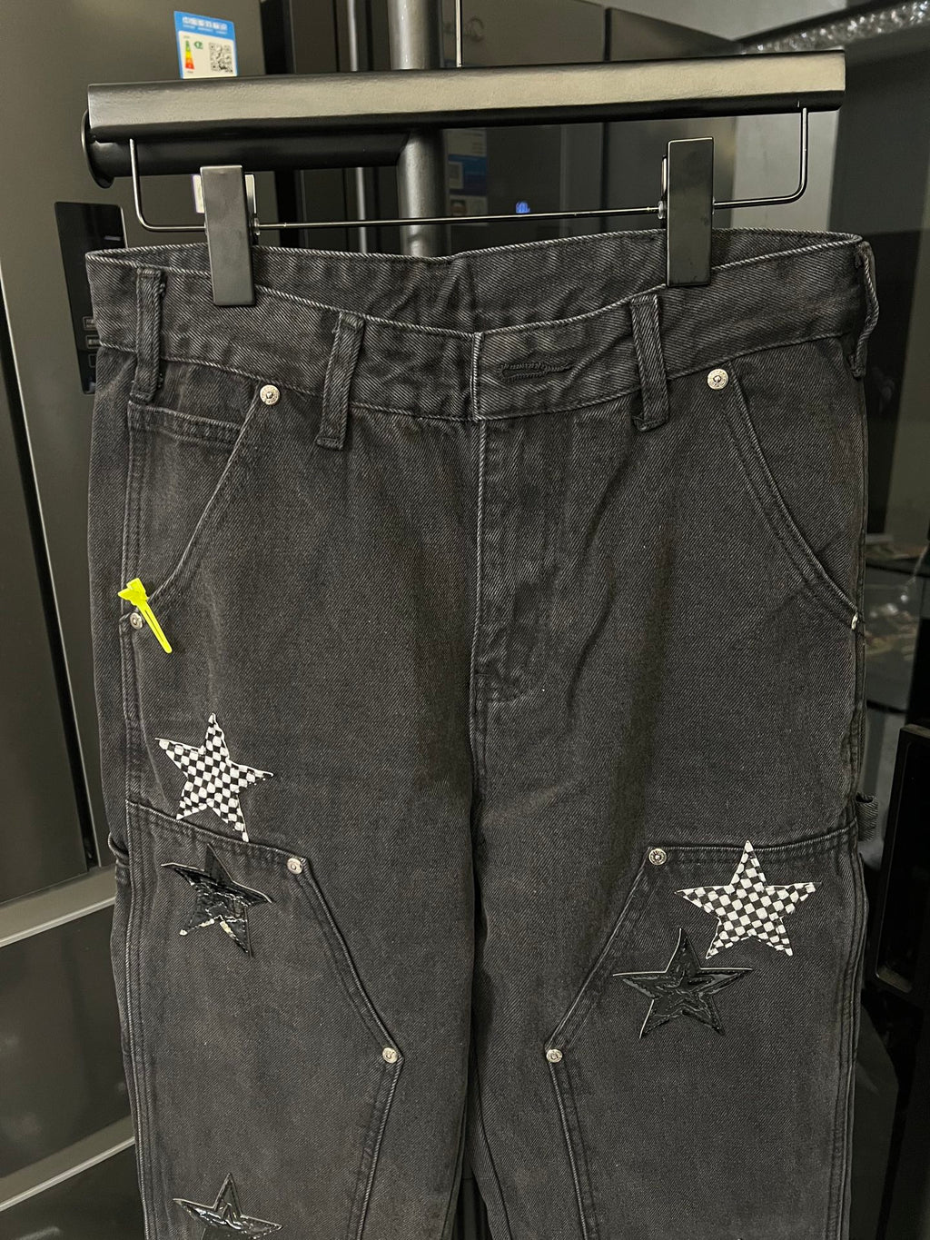 Dark gray denim pants with stitched star patches and metal buttons at pockets